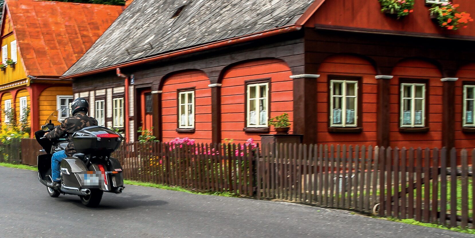 Motorrad mit Topcase vor einem roten Holzhaus mit Lattenzaun und Blumenkästen