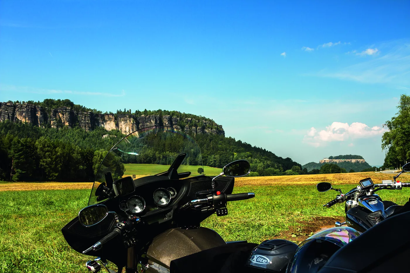 Motorräder am Straßenrand, dahinter ein bewaldetes Sandstein-Plateau