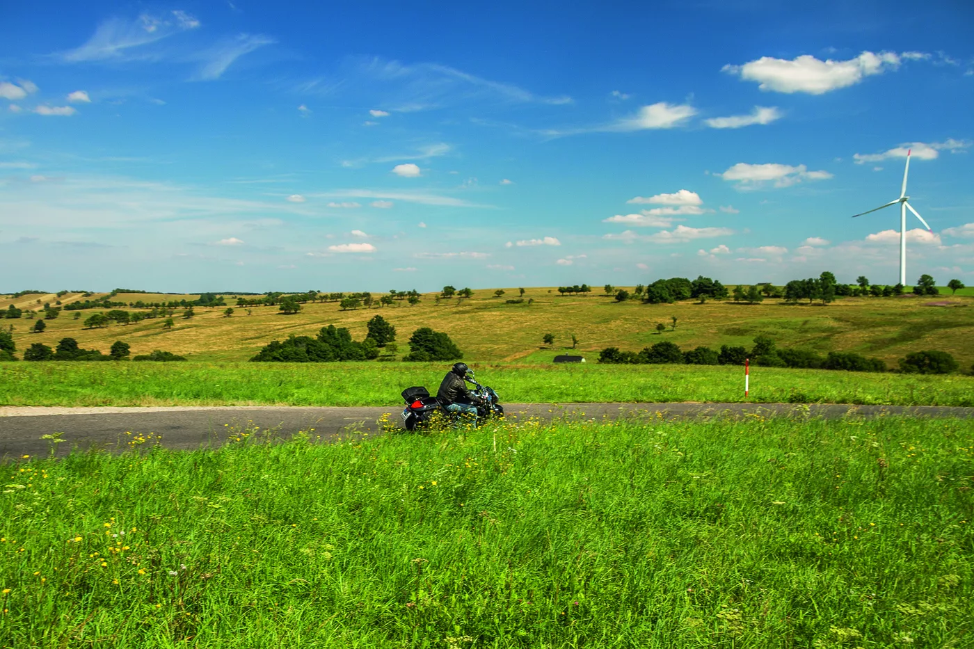 Weite Wiesenlandschaft mit einzelnem Motorrad auf der Straße